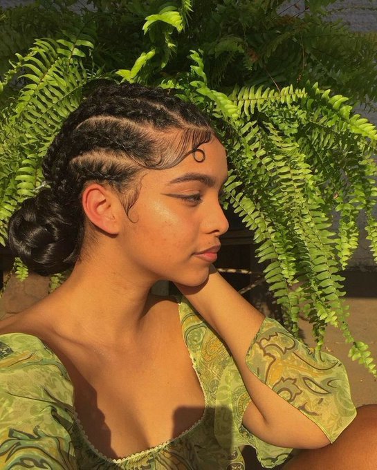 The image features a woman with her hair styled in braids, wearing a green dress that matches the leaves of a plant behind her head. The background includes a potted plant and a chair, suggesting an indoor setting or perhaps a garden-like environment. The caption reads "happy new week anons may usdt locate us", which could be interpreted as a humorous statement about how people with similar appearances might find it difficult to be recognized in certain situations.

The woman's hairstyle is styled in braids, and she has her hair tied up behind her head using a bun or ponytail. The green dress complements the leaves of the plant, creating an interesting visual connection between the woman and her surroundings.
