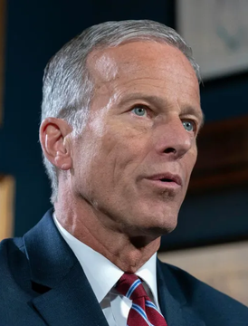 Senator John Thune is shown in a close-up portrait wearing a dark suit and striped tie, likely during a televised interview or press appearance. The image accompanies a breaking news report about his promise to allow a "risk-free" vote on the Clarity Act.