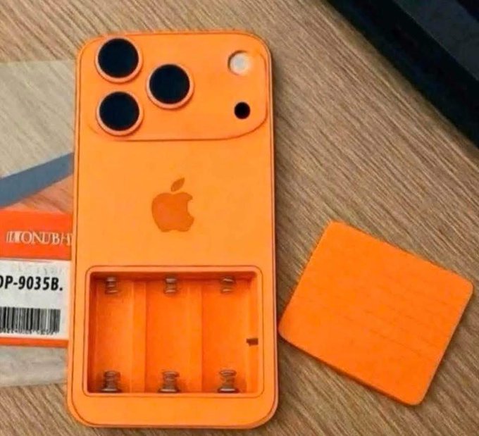 An orange novelty item resembling an iPhone with three camera lenses and an Apple logo, featuring an open battery compartment with springs, next to an orange battery cover on a wooden surface.