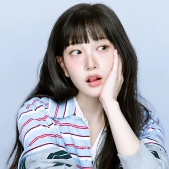 A young woman with long dark hair and bangs rests her hand against her cheek while looking off to the side, wearing a striped pastel hoodie against a light background.