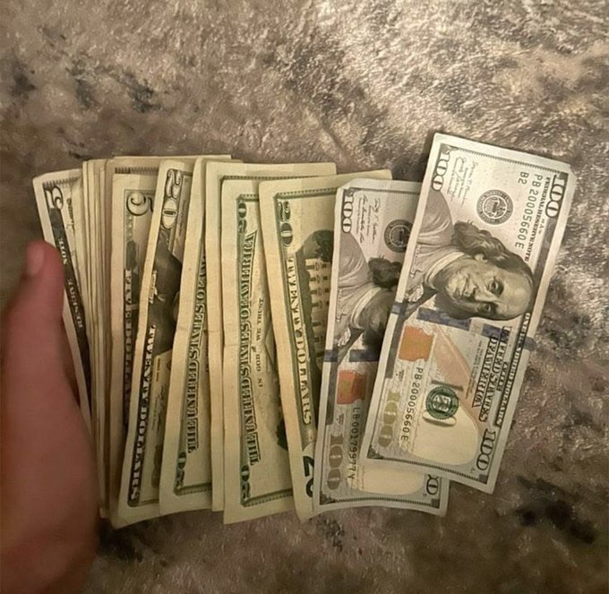 A hand fans out a spread of U.S. currency—$5, $10, $20, $50, and $100 bills—on a marbled countertop, visually reinforcing the "We're making money this week" caption with a tangible display of cash earnings.