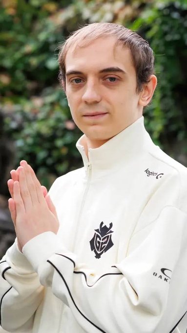 A man with short hair wearing a white jacket with an Oakley logo stands with his hands pressed together in a praying gesture.