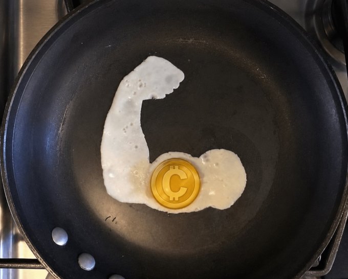 A black frying pan on a stovetop containing white liquid (likely batter or egg white) shaped like a flexing bicep, with a gold coin featuring a 'C' symbol placed as the dumbbell.
