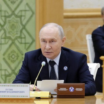 Vladimir Putin sits at a table with a nameplate reading 'ПУТИН ВЛАДИМИР ВЛАДИМИРОВИЧ' in a formal meeting setting.