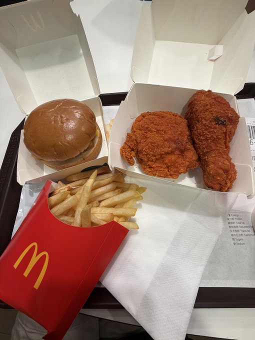 A McDonald's meal on a tray featuring a burger, fried chicken pieces in a box, and a carton of French fries with the golden 'M' logo.