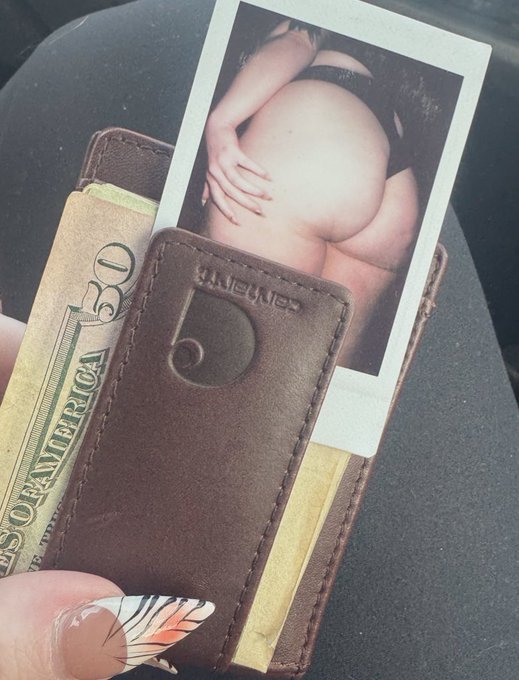 A brown leather money clip holds a $50 bill and a provocative photo of someone's rear end, fitting the sentiment of "oh to be in someone’s wallet." The Carhartt logo is visible on the money clip.