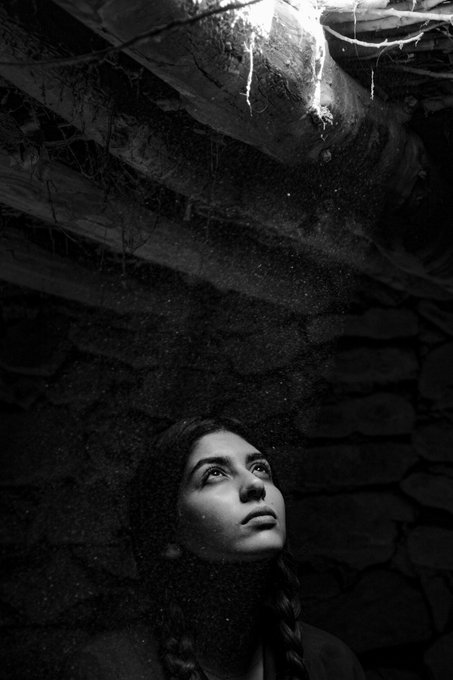 A black and white photo of a woman gazing upward in a dark, cave-like setting with light filtering down from above.