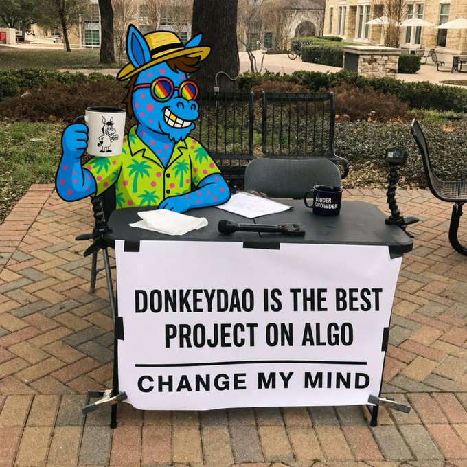 An outdoor display features a blue cartoon donkey character wearing sunglasses and a Hawaiian shirt sitting at a table with a sign reading 'DONKEYDAO IS THE BEST PROJECT ON ALGO - CHANGE MY MIND'.