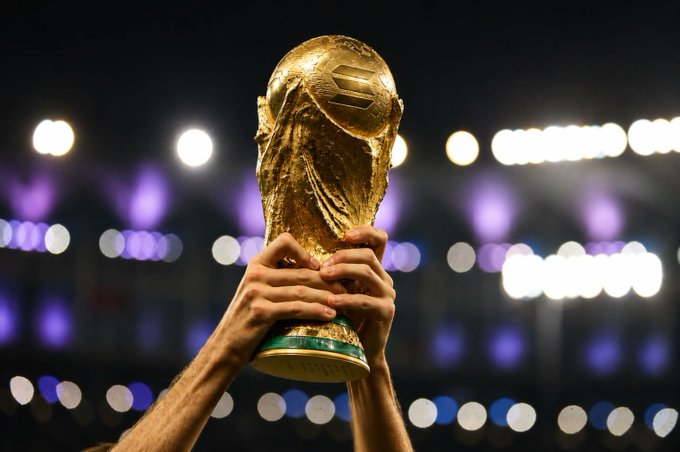 A pair of hands triumphantly hoists the FIFA World Cup trophy aloft against a stadium backdrop illuminated with lights. The image symbolizes victory and achievement, aligning with the post's theme of the Solana ecosystem enabling real-time predictions and participation during World Cup matches.