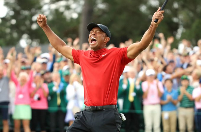 Tiger Woods, wearing a red Nike shirt and black cap, raises his arms in a triumphant victory pose while an enthusiastic crowd cheers in the background.

Note: The image shows a victorious golf moment and does not appear to relate to the cryptocurrency contract address mentioned in the accompanying text about DebtReliefBot (DRB).