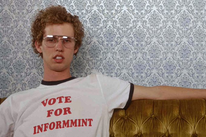 Photo of a young man with curly hair and glasses wearing a white t-shirt that reads 'VOTE FOR INFORMMINT' in red letters, sitting against a patterned wallpaper with a gold tufted chair.