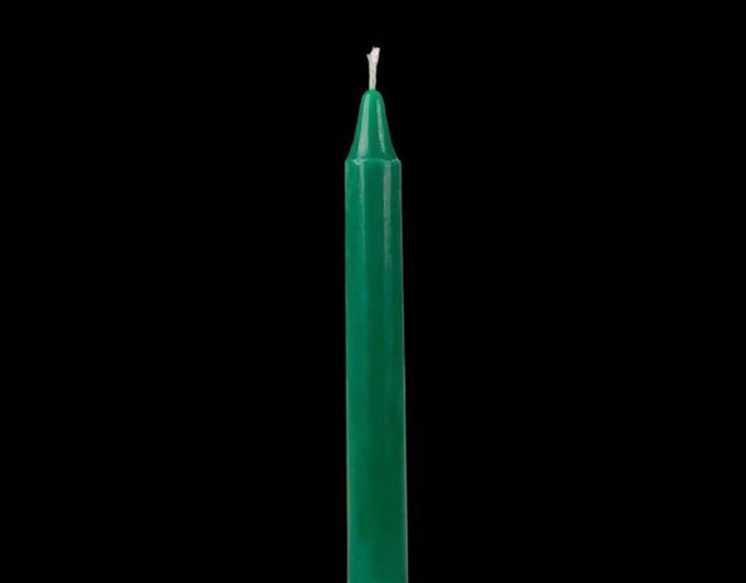 A close-up of a green candle against a black background, with a small flame visible at the wick.