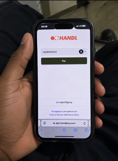 A close-up photograph of a hand holding a smartphone displaying the HANDL app login screen at app.handlpay.com, with the username "royalhunters4" entered and a green "Pay" button visible.