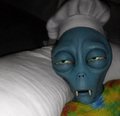A small blue alien-like figurine with large eyes, wearing a colorful rainbow tie-dye outfit.