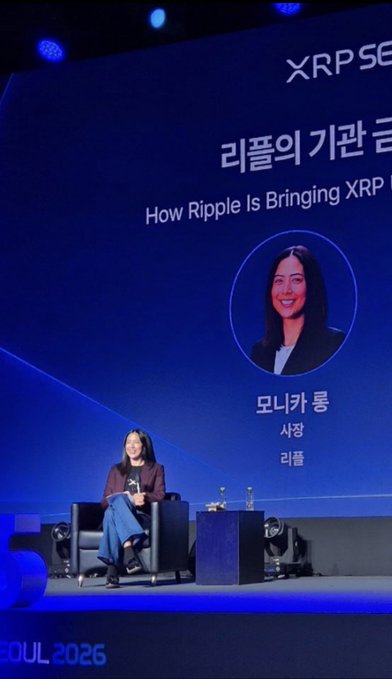 A woman sits on stage at an XRP Seoul 2026 event, with a large screen behind her reading 'How Ripple Is Bringing XRP' and identifying her as Monica Long, President of Ripple.