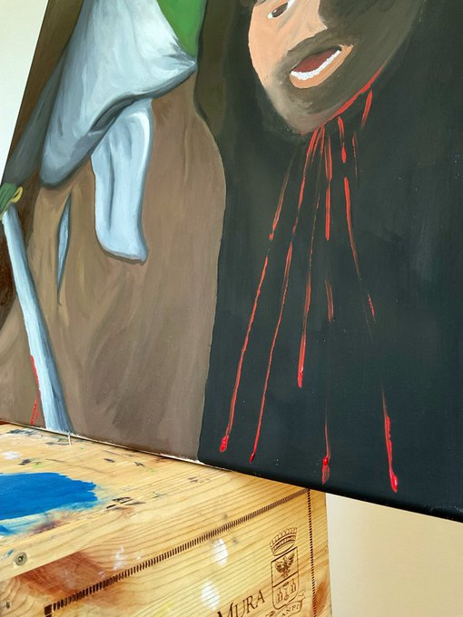 A close-up view of an in-progress painting on a wooden surface depicting a man with blood dripping down his black robe and a sword or staff with a white cloth.