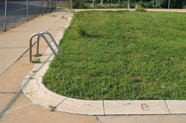 A curved sidewalk next to a grassy area with a metal bike rack and a chain-link fence.