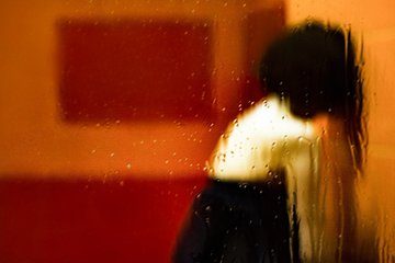A blurry, motion-filled image of a person in a white top and dark skirt leaning against an orange wall, with light streaks suggesting movement.