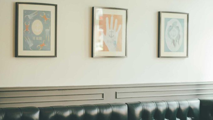 Three framed posters hang on a light-colored wall above a black tufted leather booth, with the left poster reading 'THE END IS NIGH.'