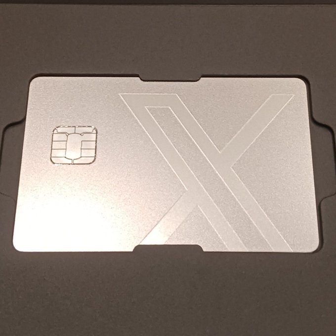 A silver metallic card with an embedded chip and a large engraved 'X' logo, resting in a black packaging tray.
