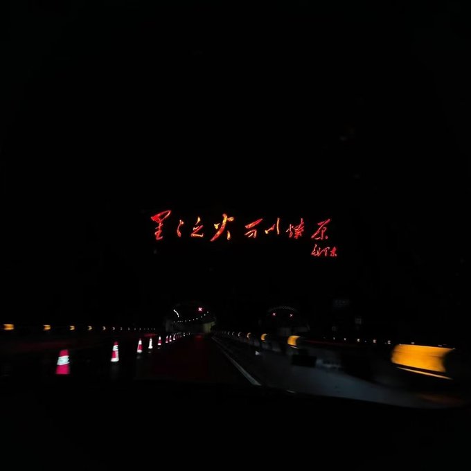A dark, nighttime photo taken from inside a tunnel or underpass, showing road barriers and a red sign with Korean text.