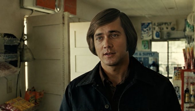 A cinematic still of actor Jared Leto with a bowl haircut wearing a dark jacket in what appears to be a convenience store setting.