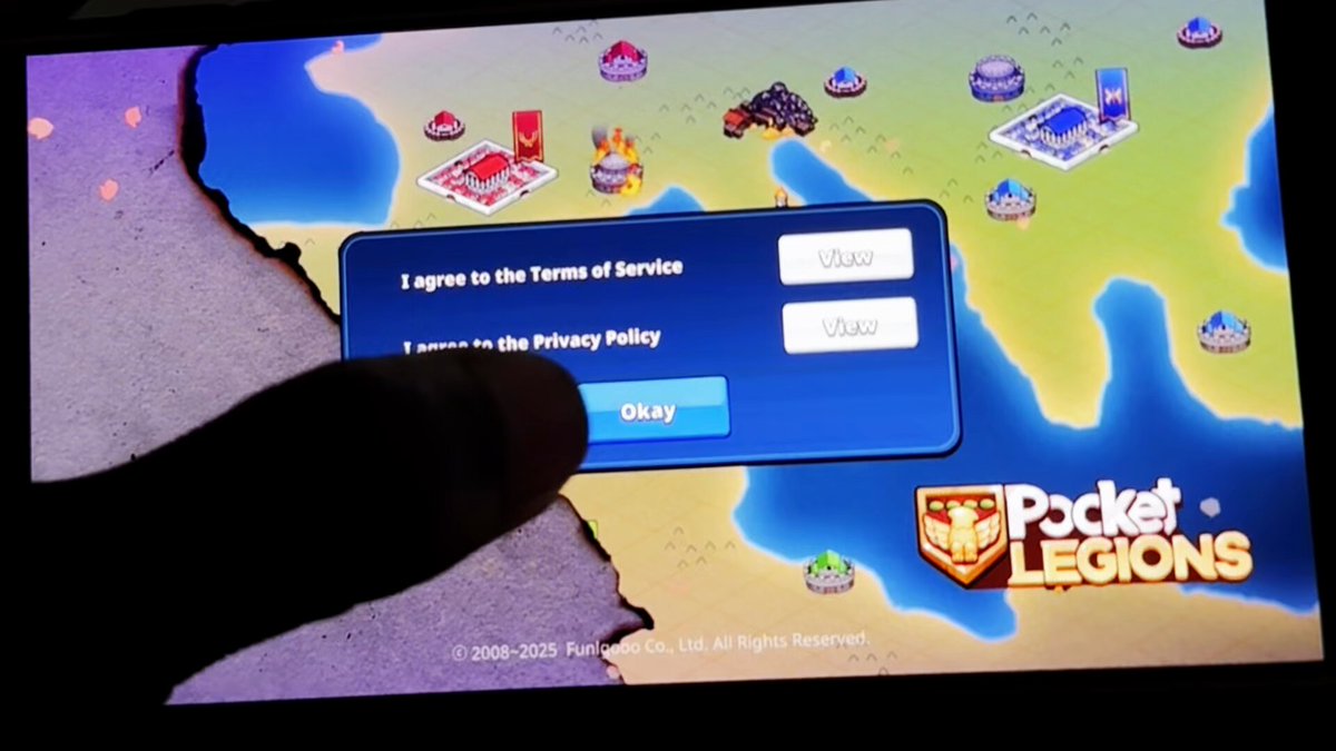 The image shows a person's finger pointing at a screen displaying a sign that says "I Agree to the Terms of Service". The person is using their finger to click on the button, indicating they have accepted the terms and conditions for the game.