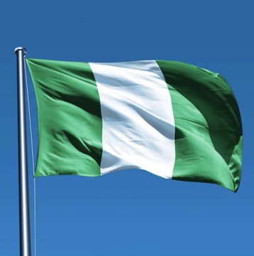 The Nigerian flag waving against a clear blue sky, featuring vertical green-white-green stripes.