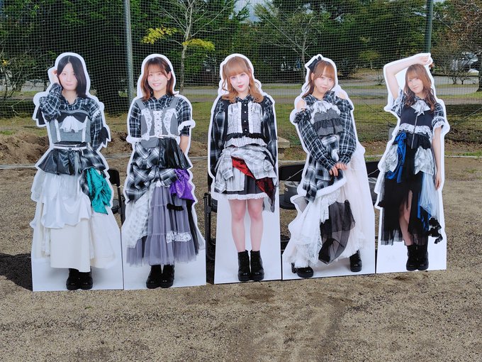 Five life-sized cardboard cutouts of women in coordinated black and white plaid and dress outfits displayed outdoors on a dirt area.