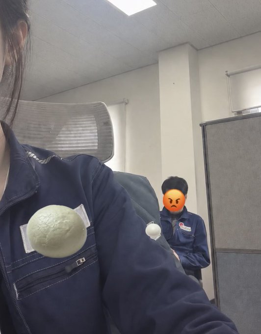 In a dimly lit office at 11:11 p.m., an exhausted worker in a navy work uniform with a balled-up object taped to the chest stares blankly at the camera, while a colleague (face covered by an angry emoji) in a similar uniform sits in a cubicle behind them, embodying the looming "section chief" the tired employee desperately wishes would finally leave so they can rest in peace.