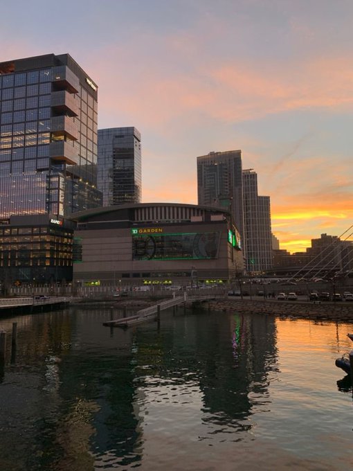 The image shows a beautiful cityscape at sunrise, featuring tall buildings reflecting the warm hues of the sky as the sun rises above them. The scene captures the essence of a new day filled with opportunities for growth and connection within the community. The caption emphasizes the importance of consistently engaging in positive habits to build a better life, just like how small actions can lead to significant results over time.