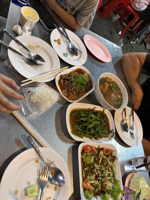 A table spread of Asian cuisine including stir-fried greens, braised meat, and soup served with chopsticks and spoons at a restaurant.