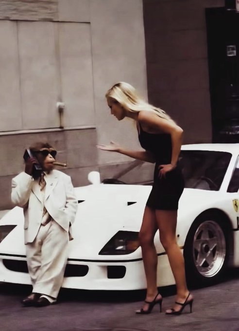 A vintage-style photograph showing a short man in a white suit and sunglasses on a phone leaning against a white Ferrari, gesturing toward a tall blonde woman in a black dress and heels.