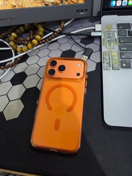 The image features a cell phone with an orange case sitting on top of a black mouse pad, which is placed on a desk or table. The background includes a laptop computer and some beads, suggesting that this scene takes place in a workspace or home office setting. The caption reads "为什么我和静香 @btc_jx 是最好的朋友 因为这些东西,都是她给我买的", which implies that the cell phone and beads might be related to Bitcoin or a similar digital currency.