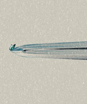 A minimalist close-up photograph of a clear, broken glass tube or rod lying horizontally on a textured white surface.