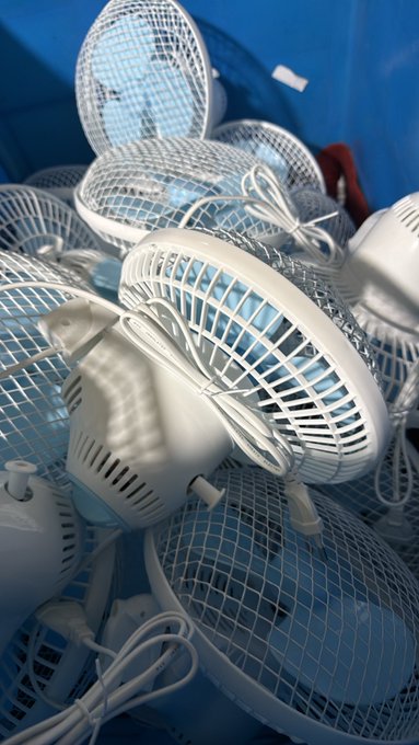 A close-up photograph displays a pile of small white electric fans with blue blades, tangled with their power cords.