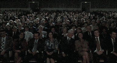 The image shows a large group of people sitting down, possibly at an event or gathering. They are all dressed formally, with some wearing ties as well. The audience appears to be engaged and attentive, likely listening to a speaker or performer on stage. The scene suggests that this could be a conference, seminar, or other formal event where attendees have gathered for a presentation or discussion.