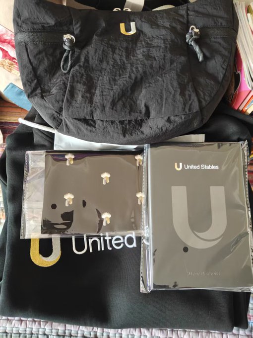 A black drawstring bag and merchandise items branded with the 'United' and 'United Stables' logos featuring a stylized 'U' with a smile.