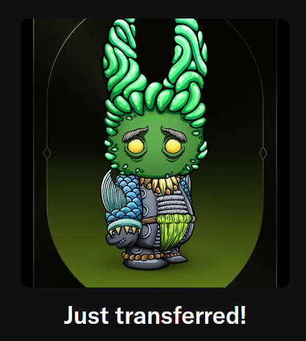 A cartoon-style green monster figurine with tall ear-like protrusions, yellow glowing eyes, and armored blue and gray detailing, displayed with the text 'Just transferred!' at the bottom.
