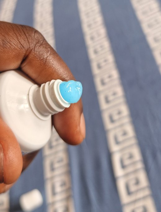A close-up shows a hand dispensing or holding a small amount of glossy light-blue gel from a white bottle over blue-and-white patterned fabric.