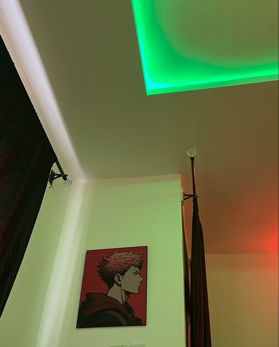 A low-angle shot of a room with green LED ceiling lights, showing a framed anime-style poster of a red-haired character on a green wall.