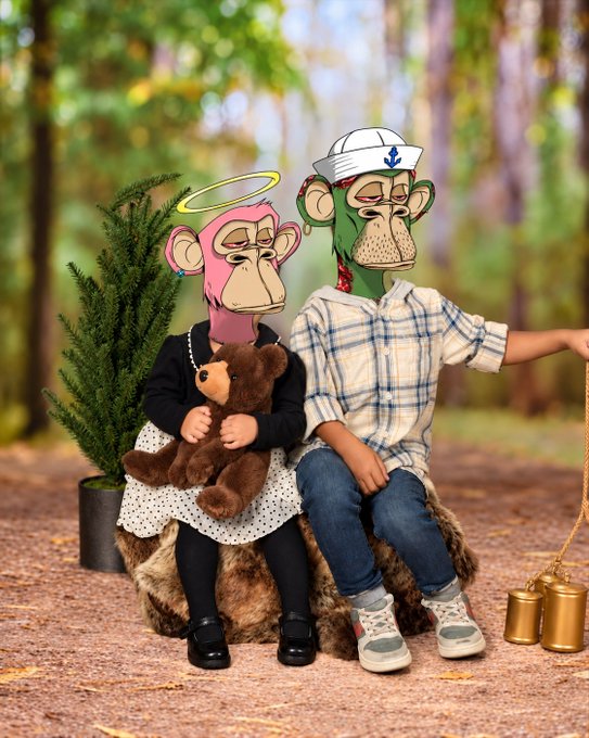 Two plush Bored Ape figurines styled as a couple sit on a log in a forest setting; the pink ape wears a polka-dot skirt and holds a teddy bear, while the green ape wears a sailor hat and plaid shirt.