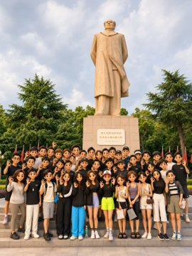 A large group of people posing for a photo in front of a tall stone statue of a robed figure in an outdoor setting.
