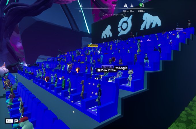 A first-anniversary celebration of @OthersideMeta is depicted in a virtual amphitheater filled with diverse avatars seated on bright blue tiered bleachers, with one username "ItsAngle" highlighted and UI elements like "Pulse District" visible above. The screen above the crowd displays stylized logos, reinforcing the milestone event showcased in the accompanying post.