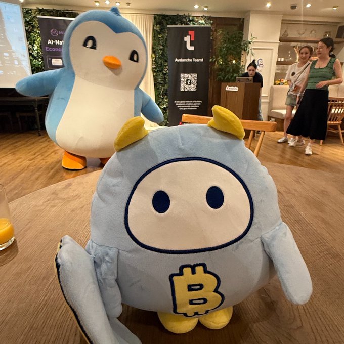 Two cute mascots, including a blue Bitcoin-themed plush with a 'B' logo and a penguin, are displayed at an Avalanche Team1 event.