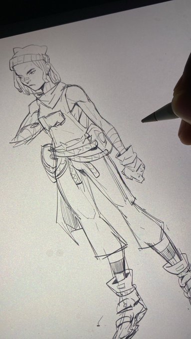 A pencil sketch of a character wearing a beanie and scarf is being drawn on paper, with the artist's pen visible at the edge.