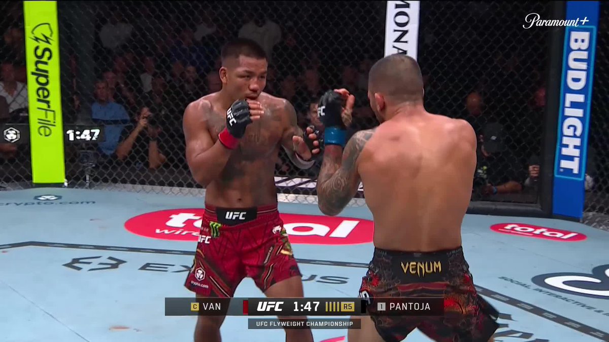 Two MMA fighters face off in a UFC octagon during the UFC Flyweight Championship, with the on-screen graphics showing "C VAN" vs "D PANTOJA" with 1:47 remaining in round R5. The cage is surrounded by sponsor banners including Superfile, Bud Light, and Toyota.