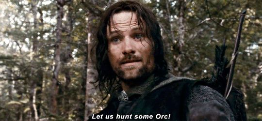 A man with long dark hair in a forest setting, with subtitle reading 'Let us hunt some Orc!'