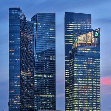 Two illuminated glass skyscrapers of Standard Chartered's headquarters stand against a twilight sky, with a green logo visible on the right tower, symbolizing the banking giant's new venture into cryptocurrency custody services for institutional clients in Singapore.