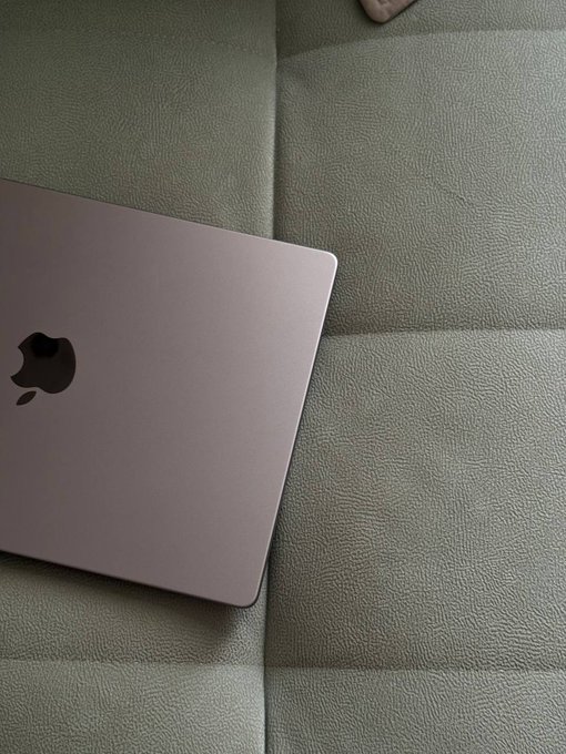 A pink Apple MacBook resting on a gray leather sofa, viewed from above.